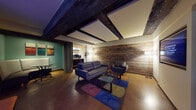 This single-floor space showcases a compelling blend of industrial character and contemporary design. The centerpiece lounge area makes an immediate impression with its exposed dark wooden ceiling beams, reclaimed wood accent wall, and polished concrete floors. Leather sofas and armchairs are arranged around a glass-topped coffee table, anchored by a colorful geometric area rug that adds a vibrant contrast to the earthy tones of the room. Warm floor lamps cast an inviting ambient glow throughout. A small kitchenette or refreshment bar is accessible from the lounge, featuring dark cabinetry and a coffee station, ideal for convenience. A cozy banquette dining nook with teal-painted walls adds an additional casual seating option. The corridors are thoughtfully designed with neutral-toned carpeting, flush ceiling fixtures, and decorative artwork adorning the walls, contributing to a polished and welcoming atmosphere. A dedicated laundry room is equipped with multiple washers and dryers alongside a vending machine, offering practical on-site amenities. The floorplan also reveals a well-equipped fitness area with a variety of exercise machines. Throughout the space, the design successfully marries raw industrial elements with refined, modern furnishings to create a cohesive and functional environment.
