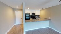 Located at 3710–3810 Wabash Avenue in San Diego's vibrant 92104 zip code, Unit 120 is a single-floor residence that blends modern updates with a functional, open layout. The kitchen is a standout feature, showcasing crisp white cabinetry, a mosaic tile backsplash, stone-finish countertops, and black appliances including a refrigerator, range, and built-in microwave. A peninsula counter extends outward, providing additional prep space and a natural division between the kitchen and the adjoining living area. The flooring throughout is a warm wood-style laminate that adds continuity and a clean, contemporary feel to the space. The living area is open and well-proportioned, featuring a large window that invites natural light and a wall-mounted HVAC unit for climate control. Neutral-toned walls throughout complement the modern finishes and provide a versatile backdrop. Recessed lighting in the kitchen adds a polished touch, while white baseboards and trim offer a crisp contrast to the flooring. The unit's single-floor layout ensures easy accessibility and a straightforward flow from the entry through the main living spaces. Overall, the residence presents a refreshed, move-in-ready interior in a well-situated San Diego neighborhood.