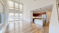 Located at 2121 S Broadway in Denver's vibrant South Broadway corridor, this modern two-story residence impresses with its dramatic double-height ceilings and expansive windows that flood the main living area with natural light. Light-toned hardwood flooring flows throughout the open-concept main level, seamlessly connecting the generous living area to the kitchen. The kitchen is outfitted with rich walnut-toned cabinetry, a white subway tile backsplash, stainless steel appliances including a French door refrigerator and range, and a central island with a sink — ideal for both everyday cooking and entertaining. A glass door off the living area opens to a private balcony, offering views of the surrounding neighborhood. Upstairs, the bedrooms feature plush carpeting, ample natural light through roller-shaded windows, ceiling fans, and double-door closets, providing comfortable and functional private retreats. The bathroom is elegantly finished with wood-toned cabinetry, a neutral stone countertop, large-format tile, and a frameless glass-enclosed soaking tub and shower combination with matte black fixtures. Clean white walls and modern trim details throughout give the entire space a crisp, contemporary feel.