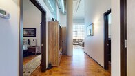 Located at 675 N Main St in the heart of downtown Winston-Salem, NC, this one-bedroom, one-bathroom loft showcases the character of an industrial conversion with thoughtfully modern updates. Rich, original hardwood floors run throughout the open-plan living space, complemented by soaring ceilings with exposed cylindrical support columns and overhead ductwork that celebrate the building's heritage.

The combined kitchen and living area forms the heart of the unit. The kitchen is outfitted with dark espresso cabinetry, granite countertops, stainless steel appliances, and a breakfast bar — functional and refined. The living area is anchored by dramatic floor-to-ceiling factory-style windows that flood the space with natural light and frame expansive views of the surrounding cityscape.

The generously sized bedroom offers a comfortable retreat with high ceilings, warm hardwood flooring, and direct access to the full bathroom. The bathroom features clean, neutral tile, a pedestal sink with granite accents, and a shower-tub combo. A dedicated laundry closet with stacked washer and dryer adds everyday convenience, while a separate closet provides additional storage. The overall ambiance balances urban industrial character with warm, livable comfort throughout.