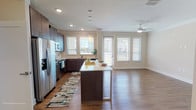 This well-appointed single-floor residence offers three bedrooms and two bathrooms across a generously sized, thoughtfully designed layout. The entryway welcomes residents through a clean, minimalist foyer finished with warm wood-style flooring that extends throughout the home, creating a cohesive and inviting aesthetic.

The open-concept kitchen is a standout feature, equipped with dark espresso cabinetry, light quartz countertops, stainless steel appliances—including a refrigerator, range, microwave, and dishwasher—and a central island with pendant lighting above. A double sink sits beneath dual windows, filling the space with natural light and exterior views. The kitchen flows seamlessly into the living area, which is brightened by large windows and a sliding glass door leading to a balcony, with a ceiling fan overhead.

The bedrooms are comfortably sized, each featuring wood-style flooring, neutral walls, and ceiling fans. Natural light enters through blinds-fitted windows. The two bathrooms are finished with large-format tile; one includes a glass-enclosed walk-in shower, while the other offers a soaking tub with tiled surround and brushed nickel fixtures. A dedicated laundry room with full-size washer and dryer adds everyday convenience.