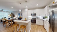 Located at 12231 Pioneers Way in Orlando, FL, this thoughtfully designed single-story residence showcases a contemporary aesthetic with warm wood-look flooring flowing throughout. The kitchen is a standout feature, outfitted with crisp white shaker cabinetry, quartz countertops, a classic subway tile backsplash, stainless steel appliances, and a central island with bar seating illuminated by pendant lighting — ideal for both cooking and casual dining. Open shelving adds a modern, functional touch. The adjoining dining area and living room offer a comfortable, connected layout, with the living space benefiting from large windows that invite abundant natural light. The primary bedroom is a serene retreat featuring multiple windows with sheer drapery and light-filtering blinds, complemented by light wood flooring. A well-appointed bathroom with a dual-sink vanity, quartz countertops, and a glass-enclosed shower serves the space in style. A second bedroom with a bold accent wall and double-door closet provides additional versatility. A dedicated laundry area with full-size washer and dryer adds everyday convenience. Neutral tones throughout create a cohesive, move-in-ready atmosphere.