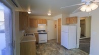 This multi-floor space spans three levels, offering a practical and straightforward layout. The kitchen is equipped with essential appliances, including a white gas range with an overhead ventilation hood, a full-size refrigerator, and a stainless steel sink. Warm-toned wood cabinetry lines the walls, providing generous storage space above and below the countertops. The neutral-toned countertops complement the cabinetry, creating a cohesive look throughout the kitchen. Stone-patterned flooring adds a durable and easy-to-maintain surface underfoot, while flush-mount ceiling light fixtures ensure the space is well-lit. A fire extinguisher is visibly mounted near the doorway, reflecting attention to safety. The kitchen connects to additional areas of the unit through a doorway, facilitating easy flow between spaces. The overall design is straightforward and functional, prioritizing practicality across all three floors. The light-colored walls and ceiling contribute to a clean, neutral atmosphere throughout the space.