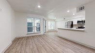 This single-floor residence showcases a clean, modern design with an open-concept living and kitchen area at its core. Light wood-style vinyl flooring runs throughout the entire unit, creating a cohesive and contemporary aesthetic. Crisp white walls and recessed lighting enhance the bright, airy atmosphere across all spaces.

The open living area is well-lit by multiple large windows fitted with horizontal blinds, allowing generous natural light to fill the space. A sliding glass door provides additional light and outdoor access. The kitchen is positioned along one side of the open layout and features white shaker-style cabinetry, a stainless steel refrigerator, microwave, and dishwasher, along with a peninsula countertop that offers both prep space and a natural divider between the kitchen and living areas.

The bedroom is a calm, well-proportioned space with a ceiling fan, a window overlooking greenery, and the same consistent flooring found throughout the unit. The bathroom is finished with subway tile surrounding a full soaking tub and shower combination, complemented by white cabinetry above the toilet and wood-style flooring that ties back to the rest of the home.