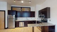 Situated along North Main Street in the heart of downtown Winston-Salem, North Carolina, this modern single-floor unit offers a thoughtfully designed open layout with contemporary finishes throughout. Light hardwood flooring flows seamlessly across the main living areas, complemented by bold black trim that adds a clean, urban aesthetic.

The kitchen is a standout feature, equipped with rich dark espresso cabinetry, granite countertops, and a full suite of stainless steel appliances including a refrigerator, electric range, over-the-range microwave, and dishwasher. A granite-topped breakfast bar provides additional counter space and a casual dining option. Track lighting overhead ensures the kitchen is both functional and well-lit.

The open living area is bright and airy, with large windows fitted with blinds that invite natural light while offering street views of downtown. A ceiling fan adds comfort to the space.

The bedrooms are generously proportioned, each featuring hardwood floors, ceiling fans, and interior clerestory windows that borrow light from adjoining spaces. The unit includes two bathrooms: one with a striking dark vanity and a distinctive glass vessel sink paired with a tub-shower combination, and a second full bath with a clean, straightforward design. The overall ambiance is modern, minimal, and well-suited to urban living.