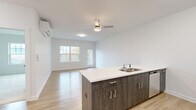 Located at 255 Cemetery Rd in Troy, NY, this thoughtfully designed 2-bedroom, 1-bathroom residence offers a clean, modern aesthetic across a single level. The heart of the home is an open-concept kitchen and living area anchored by a large center island with a white quartz countertop and dark wood-finish cabinetry. The kitchen is equipped with stainless steel appliances, including a refrigerator, range, and microwave, complemented by light gray upper cabinets. Light-toned luxury vinyl plank flooring runs throughout the main living areas, enhancing the bright, airy feel created by white walls and a ceiling fan with integrated lighting. A wall-mounted mini-split system provides efficient climate control. The living area opens to a private balcony with a white-railed deck, offering expansive views of the surrounding neighborhood and rolling landscape beyond. Both bedrooms feature plush carpeting, ample natural light from large windows, and dedicated closet spaces with wire shelving systems. The primary bedroom is a comfortable, well-proportioned retreat. The full bathroom is finished with light wood-look flooring, a vanity with white countertop, and a tub/shower combination. A hallway connects all rooms, maintaining a practical and efficient layout throughout.