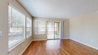 Located at 5905 30th Avenue West in Bradenton, Florida, this single-floor, one-bedroom, one-bathroom unit offers a well-designed layout that maximizes its cozy footprint. The open-plan kitchen and living room form the heart of the space, where warm hardwood-style flooring flows throughout. The kitchen is appointed with rich wood cabinetry, dark granite-style countertops, a breakfast bar peninsula, and black appliances, including a refrigerator and electric range. A pendant light and flush-mount fixture provide ample illumination. The living area features a textured ceiling, a ceiling fan, and sliding glass doors that invite natural light and provide access to an outdoor area, creating a seamless indoor-outdoor connection. The spacious primary bedroom is carpeted for comfort, offers its own ceiling fan, and features sliding glass doors that also open to the outdoors, along with a dedicated closet with louvered bifold doors. A secondary closet is conveniently located near the entry. The bathroom includes a full tub-shower combination with clean white surrounds and hardwood-style flooring. Neutral warm-beige walls, abundant natural light from multiple windows with blinds, and recessed lighting throughout contribute to a bright, welcoming ambiance throughout the home.