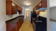 Located at 12901 CR-5 W in Burnsville, Minnesota, this single-floor unit offers a practical and comfortable layout designed for everyday living. The galley-style kitchen is a standout feature, showcasing rich dark wood cabinetry, dark granite countertops, a stainless steel sink, and black appliances including an electric range and refrigerator. Light wood-look flooring runs throughout the kitchen, adding warmth and continuity to the space.

The living area is bright and open, featuring durable wood-look flooring, a sliding glass door with vertical blinds that brings in natural light and provides access to an outdoor view, and a wall-mounted air conditioning unit alongside baseboard heating for year-round comfort. A ceiling fan adds additional airflow to the space.

The bedroom is a quiet retreat finished with plush carpet and a window with blinds, allowing for natural light while maintaining privacy. Baseboard heating ensures comfort during Minnesota's colder months.

The full bathroom is clean and functional, featuring white square tile surrounding a bathtub and shower combination, wood-look flooring, and warm wood-toned door trim that adds a touch of character. Additional areas include an entry space with wood-look flooring that connects seamlessly to the rest of the unit. Textured ceilings are consistent throughout, contributing to the overall classic residential aesthetic of this Burnsville home.