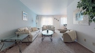 Located on Beech Road in Southfield, Michigan, this single-floor unit offers a well-organized and functional layout across several distinct living areas. The living room serves as the heart of the home, featuring soft carpeted flooring, a calming blue accent wall, and multiple windows dressed with vertical blinds that allow generous natural light to fill the space. The open and airy feel is complemented by a glass-top coffee table and comfortable seating arrangements.

Adjacent to the living room is a dedicated dining area with hardwood flooring, a ceiling fan, and a round glass-top dining table surrounded by elegant wrought-iron chairs — ideal for casual meals or entertaining.

The galley-style kitchen is efficiently designed with dark wood cabinetry lining both sides, white countertops, hardwood flooring, and standard appliances including a range, refrigerator, and dishwasher, with a convenient pass-through to additional living space.

The bedrooms are carpeted and well-lit, each offering closet storage. The primary bedroom features dual bi-fold closets and access to a walk-in shelving area, along with a ceiling fan. A secondary bedroom provides a bright window with natural light.

The full bathroom includes a combination tub and shower with glass sliding doors, dark wood vanity cabinetry, a white countertop, and classic mosaic tile flooring.