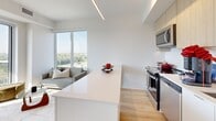 Located on the 9th floor at 610 Martin Grove Road in Toronto's west end, this thoughtfully designed two-bedroom, two-bathroom unit offers a bright and contemporary living experience. The open-concept kitchen anchors the main living area, featuring light wood cabinetry, stainless steel appliances, a clean white quartz island with bar seating, and track lighting overhead — all flowing seamlessly into the living space, which is bathed in natural light from large floor-to-ceiling windows with expansive treetop and city skyline views. Light hardwood flooring runs throughout, reinforcing the unit's airy, modern aesthetic. The primary bedroom is a well-proportioned retreat complete with a large sliding-door closet and a window framing open views of the surrounding neighbourhood and Toronto skyline. The second bedroom offers equally comfortable accommodations with its own sliding-door closet and a serene, understated atmosphere. Both bathrooms are finished with large-format neutral tile; one features a deep soaking tub with overhead shower, while the other offers a clean walk-in shower stall with a matching vanity. A private balcony extends the living space outdoors, offering sweeping views of lush greenery and the broader cityscape beyond.