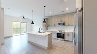 This thoughtfully designed one-bedroom, one-bathroom residence in North Chesterfield, VA offers a clean, contemporary aesthetic throughout its efficiently laid-out single floor. The open-concept kitchen serves as the heart of the home, showcasing two-tone cabinetry in warm taupe and light gray, a classic white subway tile backsplash, stainless steel appliances including a French door refrigerator and electric range, and a central island with a white quartz countertop, undermount sink, and stylish matte black pendant lighting overhead. Light wood-tone luxury vinyl plank flooring extends seamlessly through the kitchen and living areas, enhancing the bright, airy feel of the space. The living room opens directly to a private balcony through sliding glass doors, offering treetop views and filling the room with natural light. A ceiling fan adds comfort to both the living and bedroom spaces. The bedroom features soft carpeting, a dedicated ceiling fan, a window with outdoor views, and access to the well-appointed bathroom. The bathroom is finished with a long dual-sink vanity, white quartz counters, a glass-enclosed walk-in shower with tile surround, and direct access to a built-in closet with shelving. A hallway connects the private quarters to the main living areas, completing this modern and functional residence.