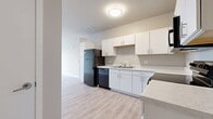 Located at 1300 N Lancaster Rd in South Elgin, IL, this 3-bedroom, 2-bathroom apartment spans 1,060 square feet across a single floor, offering a functional and modern living environment. The kitchen features white cabinetry with sleek hardware, light-colored countertops, a double stainless steel sink, and a full suite of black appliances including a refrigerator, electric range, built-in microwave, and dishwasher, all set on durable wood-look vinyl flooring. The open layout connects the kitchen to the living area, which is enhanced by a ceiling fan and large windows fitted with horizontal blinds that allow ample natural light. The primary bedroom measures 170 square feet and includes light wood-look vinyl flooring, a ceiling fan, and access to a spacious walk-in closet outfitted with wire shelving on three walls. The two additional bedrooms feature plush carpet and built-in double-door closets. Both bathrooms include a tub/shower combo, vanity with white cabinetry, and warm wood-look vinyl flooring. The unit's neutral color palette and clean, contemporary finishes create a bright and cohesive atmosphere throughout.