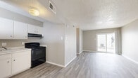 This single-floor unit offers a practical and efficient layout comprising a living room, kitchen, and bathroom. Throughout the space, wood-look plank flooring in a light gray tone provides a cohesive, modern aesthetic, complemented by neutral gray walls and clean white baseboards. A textured popcorn ceiling is consistent across the rooms, adding a classic residential character.

The living room is an open, airy space with a front entry door flanked by a window that allows natural light to filter in. A sliding glass door at the rear of the living area offers additional light and access to an outdoor area, creating a welcoming and functional gathering space.

The kitchen is positioned adjacent to the living area and features white upper and lower cabinetry offering ample storage, a single-basin sink with countertop workspace, and a black electric range with an overhead ventilation hood. The layout is straightforward and efficient, suited for everyday meal preparation.

The bathroom includes a vanity with a light-colored countertop and an integrated sink, along with an adjacent closet area with overhead shelving, providing convenient storage. The consistent wood-look flooring extends into the bathroom, maintaining a unified look throughout.

Overall, this unit presents a clean, move-in-ready interior with a neutral palette that offers flexibility for a variety of furnishing styles.