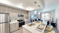 Located at 3260 Stockton Street in North Fort Myers, FL, this thoughtfully designed one-bedroom, one-bathroom residence offers a modern open-concept floor plan with stylish finishes throughout. Light wood-tone flooring flows seamlessly across the entire space, complementing the bright, neutral color palette.

The kitchen serves as a focal point, featuring light wood cabinetry extending to the ceiling, quartz countertops, a full suite of stainless steel appliances — including a refrigerator, electric range, and built-in microwave — and a centered island with a single-basin sink and pendant lighting overhead, ideal for both meal preparation and casual dining.

The open living area is bathed in natural light and connects directly to a private balcony through sliding glass doors, offering outdoor views of the surrounding greenery. A ceiling fan adds comfort to the space.

The bedroom is a serene retreat with large windows that invite abundant natural light, a ceiling fan, and access to a walk-in closet with wire shelving for generous storage.

The bathroom features light wood cabinetry, a wide quartz vanity, a large mirror, and wood-look flooring, maintaining the cohesive modern aesthetic found throughout the home.
