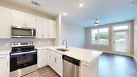This thoughtfully designed 1-bedroom, 1-bathroom unit offers a practical and modern living experience across a single floor. The open-concept kitchen and living area serves as the heart of the space, featuring wood-look luxury vinyl plank flooring that adds warmth and durability. The kitchen is outfitted with crisp white shaker-style cabinetry extending to the ceiling for maximum storage, a peninsula with a white quartz countertop and undermount sink, and a full suite of stainless steel appliances including a French door refrigerator, electric range, over-the-range microwave, and dishwasher. A tile backsplash adds a clean, polished finish. The adjacent living area benefits from a ceiling fan and a large window that frames outdoor greenery views. The bedroom is comfortably sized, finished with plush carpeting, and features a generous window with outdoor views and a dedicated closet. The bathroom maintains the home's clean aesthetic with a white shaker vanity, white quartz countertop, a framed mirror, and tile flooring. Throughout the unit, neutral warm-toned walls and recessed lighting create a bright, cohesive ambiance.