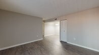 This single-story unit offers a practical and cohesive layout designed for comfortable everyday living. The main living area is finished with durable wood-style plank flooring and neutral gray-toned walls, creating a clean, modern aesthetic. A large sliding glass door fitted with vertical blinds allows natural light to fill the space and provides direct access to the outdoors. The living area flows openly into a dedicated dining space, which features a pendant light fixture overhead, enhancing functionality and visual continuity.

The kitchen is equipped with gray cabinetry, coordinating gray speckled countertops, a black electric range with coil burners and a built-in range hood above. The cabinetry provides ample storage, and the layout makes efficient use of available counter space.

The bedrooms are carpeted in a neutral tone and receive natural light through windows fitted with blinds. Both rooms offer a quiet, comfortable atmosphere well-suited for rest or use as a home office. Closet storage is accessible from the main living area.

The bathroom features a vanity with gray cabinetry and a speckled countertop that matches the kitchen's finishes, a mirror with medicine cabinet, and light wood-style flooring. Textured ceilings are present throughout portions of the unit, adding subtle architectural character to the overall interior.