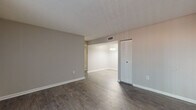 This single-story unit offers a practical and cohesive layout designed for comfortable everyday living. The main living area is finished with durable wood-style plank flooring and neutral gray-toned walls, creating a clean, modern aesthetic. A large sliding glass door fitted with vertical blinds allows natural light to fill the space and provides direct access to the outdoors. The living area flows openly into a dedicated dining space, which features a pendant light fixture overhead, enhancing functionality and visual continuity.

The kitchen is equipped with gray cabinetry, coordinating gray speckled countertops, a black electric range with coil burners and a built-in range hood above. The cabinetry provides ample storage, and the layout makes efficient use of available counter space.

The bedrooms are carpeted in a neutral tone and receive natural light through windows fitted with blinds. Both rooms offer a quiet, comfortable atmosphere well-suited for rest or use as a home office. Closet storage is accessible from the main living area.

The bathroom features a vanity with gray cabinetry and a speckled countertop that matches the kitchen's finishes, a mirror with medicine cabinet, and light wood-style flooring. Textured ceilings are present throughout portions of the unit, adding subtle architectural character to the overall interior.