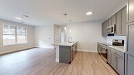 This well-appointed 3-bedroom, 2-bathroom residence in Rochester, MN offers a thoughtfully designed single-floor layout with modern finishes throughout. The open-concept kitchen and living area serves as the heart of the home, anchored by a central island with granite countertops, sleek gray shaker cabinets, a white subway tile backsplash, and stainless steel appliances including a refrigerator, range, and microwave. Pendant lighting above the island adds a contemporary touch, while light wood-look flooring flows seamlessly through the main living areas. The generously sized primary bedroom features direct access to a well-equipped bathroom appointed with matching gray cabinetry, granite countertops, a tall linen tower, and a large vanity mirror. Two additional bedrooms offer plush carpeting and natural light through large windows with exterior views. The space also includes two closets, one of which is a walk-in fitted with wire shelving. The two bathrooms maintain a cohesive, modern aesthetic consistent with the rest of the home. Clean neutral tones, crisp white trim, and an abundance of natural light lend a fresh, move-in-ready ambiance to this comfortable Rochester residence.