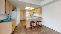 This two-story residence offers a practical and well-organized layout across both floors. The main level greets visitors with a spacious living area finished with durable wood-look flooring, neutral-toned walls, and a staircase with white balustrades leading to the upper level. The kitchen is efficiently designed with light wood cabinetry, a skylight panel for added brightness, a coil-top range, and a double sink. A peninsula counter with bar seating provides a casual dining option and connects the kitchen to the surrounding living space.

The upper level houses multiple bedrooms, each carpeted in a warm beige tone and featuring windows dressed with horizontal blinds that invite natural light. Several bedrooms include built-in closets with double doors, providing ample storage. The bathrooms are consistent in design throughout the home, featuring light wood vanity cabinetry, tile flooring in earthy tones, single-basin sinks with countertop space, and tub-shower combinations. One bathroom includes a large mirror above the vanity and a decorative shower curtain, while another offers a clean, straightforward layout. The overall aesthetic is clean, neutral, and move-in ready.