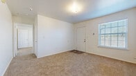 This single-floor unit offers a clean, functional layout designed for comfortable everyday living. The main living area greets occupants at the front entry, featuring soft carpeting underfoot, white walls, and a window fitted with blinds that allows natural light to filter in. A ceiling fan overhead helps maintain airflow throughout the space.

The galley-style kitchen is efficiently designed with light oak cabinetry lining both walls, offering generous storage. White laminate countertops provide ample workspace, while black appliances — including a range, refrigerator, and dishwasher — are neatly integrated into the layout. Warm wood-look flooring runs throughout the kitchen, adding visual warmth.

The living and dining area adjacent to the kitchen benefits from an open sightline, with a ceiling fan and wood-look flooring continuing the cohesive aesthetic. The bedrooms are carpeted and well-proportioned, each featuring windows with blinds that bring in natural light. One bedroom includes a ceiling fan for added comfort.

The bathroom is finished with wood-look flooring and includes a full-size soaking tub and shower combination with chrome fixtures, a toilet, and a vanity with oak cabinetry and a white countertop. Clean white walls and simple, practical finishes define the overall ambiance of this thoughtfully arranged space.
