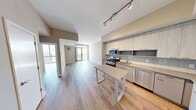 Located in the Escape building in Stamford, CT, this two-bedroom, one-bathroom residence is designed with a clean, contemporary aesthetic throughout. Light wood-style flooring runs continuously across the entire floor plan, complementing the neutral warm-gray wall tones and white trim to create a bright, cohesive atmosphere.

The combined kitchen and living area serves as the heart of the home. The kitchen is outfitted with light wood cabinetry extending to the ceiling, a soft blue glass tile backsplash, quartz-style countertops, and a full suite of stainless steel appliances including a gas range, built-in microwave, dishwasher, and a French door refrigerator with ice and water dispenser. A freestanding island provides additional prep and dining space. The open living area features a sliding glass door that leads to a private balcony with expansive elevated views of the Stamford skyline and surrounding cityscape.

The spacious primary bedroom offers generous proportions and large floor-to-ceiling windows that frame striking city views and fill the room with natural light. The second bedroom is also well-sized with its own window and access to natural light. A dedicated closet with built-in shelving and rod provides organized storage.

The bathroom features a sleek, modern vanity with an illuminated mirror, gray cabinetry, and a clean, minimalist design. An in-unit laundry closet is conveniently accessible from the bathroom hallway.
