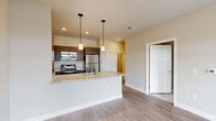 This well-appointed single-floor residence showcases a clean, modern design with a cohesive neutral color palette and quality finishes throughout. The open-concept living and kitchen area serves as the heart of the unit, where light wood-style flooring flows seamlessly underfoot. The kitchen is equipped with stainless steel appliances, including a refrigerator, range, and microwave, complemented by rich dark cabinetry, granite countertops, and a peninsula island with a undermount sink — finished off with stylish pendant lighting overhead.

The living area is bright and airy, featuring large sliding glass doors that open onto a private balcony, providing outdoor views and generous natural light. The bedrooms are carpeted for comfort, with one room featuring a ceiling fan and a large window that brings in additional natural light.

A hallway connects the living spaces to the bathroom and storage areas, with multiple white panel doors offering access to closets along the way. The bathroom is finished with a granite-topped dark vanity, a large framed mirror, and clean tile-style flooring. Throughout the unit, white baseboards, recessed lighting, and a consistent neutral wall tone contribute to a bright, polished, and inviting atmosphere.