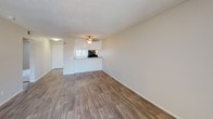Located at 1501 E Grand Ave in Escondido, California, this single-floor unit offers a practical and comfortable layout designed for everyday living. The open living area is finished with warm wood-look vinyl flooring and features a ceiling fan, textured ceiling, and a sliding glass door that leads to an outdoor balcony, allowing natural light to fill the space. A pass-through counter connects the living area to the kitchen, which is equipped with white shaker-style cabinetry, gray countertops, a stainless steel sink, and black appliances including a refrigerator, electric range with overhead exhaust, and dishwasher. The bedrooms are carpeted for comfort and warmth, each featuring neutral wall tones and ample closet space with sliding doors. Windows in the bedrooms provide views of surrounding greenery. The bathroom is well-appointed with a single-sink vanity featuring white cabinetry and a gray countertop, a large mirror, pendant lighting, and a full tub and shower combination. Wood-look flooring carries through the bathroom, tying the space together cohesively. Overall, the unit presents a clean, functional aesthetic with a neutral palette throughout.