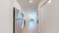 Located at 4225 SE Milwaukie Ave in Portland, Oregon, this two-bedroom, one-bathroom unit offers a clean, modern aesthetic with consistent light wood flooring and crisp white walls throughout. The open kitchen is a standout feature, equipped with a full suite of stainless steel appliances — including a refrigerator, dishwasher, electric range, and built-in microwave — complemented by sleek white cabinetry extending to the ceiling, light countertops, and recessed lighting that keeps the space bright and functional. Both bedrooms are efficiently designed with white walls and natural light from windows. The primary bedroom includes a sliding double-door closet, while the second bedroom features a wall-mounted AC/heating unit and a window with exterior views. The bathroom continues the modern minimalist theme with wood-look flooring, a white floating vanity with an undermount sink, a large mirror, and matte black hardware accents for a contemporary touch. The unit's cohesive design — uniform flooring, neutral palette, and modern fixtures — creates a clean, move-in-ready living environment in Portland's sought-after Sellwood-Moreland neighborhood.
