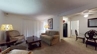 Located at 18583 Colima Rd in Rowland Heights, California, this single-floor residence offers a comfortable and functional layout with distinct living spaces throughout. The living room is generously sized, finished with wall-to-wall carpeting and a textured ceiling, and features large sliding glass doors dressed with vertical blinds that invite natural light into the space. The open arrangement accommodates multiple seating areas, creating a welcoming and versatile environment for both relaxing and entertaining. Adjacent to the living area, the galley-style kitchen is appointed with dark laminate countertops, white cabinetry, and hardwood-style flooring. Black appliances, including a refrigerator, dishwasher, and range, provide a sleek contrast, while a vertical-blind window brings in additional natural light. The bedroom is a peaceful retreat, offering generous floor space with soft carpeting, a wall-mounted air conditioning unit, and neutral walls that lend a calm, restful ambiance. The bathroom features an extended vanity with dark countertops, white cabinetry, and a wide mirror with built-in lighting, offering ample counter space. Throughout the residence, the consistent use of neutral tones and practical finishes creates a cohesive and comfortable living environment.