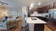 Located at 4770 Teel Pkwy in Frisco, TX, this well-appointed single-floor residence offers a thoughtfully designed open-concept layout finished with rich hardwood-style flooring and crown molding throughout the main living areas. The kitchen is a standout feature, showcasing dark espresso cabinetry extending to the ceiling, crisp white quartz countertops, a classic subway tile backsplash, and a full suite of stainless steel appliances including a French door refrigerator, range, microwave, and dishwasher. A generously sized center island with bar seating provides additional prep space and casual dining. The kitchen flows seamlessly into a dedicated dining nook framed by crown molding, and into the living room, which is brightened by natural light streaming through French doors that open to an outdoor area. The bedrooms are carpeted and serene, with neutral tones and large windows. At least one bedroom includes a spacious walk-in closet with built-in shelving. The bathrooms are finished with large-format tile surrounds — one featuring a soaking tub and shower combination, and another offering a glass-enclosed walk-in shower with wood-look tile flooring. The overall ambiance is contemporary and inviting, with consistent design details tying each space together cohesively.
