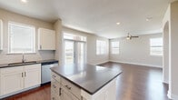 This single-floor residence offers a thoughtfully designed layout encompassing 2 bedrooms, 2 bathrooms, and 2 closets. The open-concept kitchen and living area serves as the heart of the home, featuring a central island with dark countertops, crisp white cabinetry, and a full suite of stainless steel appliances including a refrigerator, range, microwave, and dishwasher. Rich hardwood-style flooring extends throughout the main living areas, complementing the neutral warm-beige walls. The living room benefits from abundant natural light through large windows and a glass door that opens to an outdoor view, and is equipped with a ceiling fan overhead. A graceful arched doorway connects the living space to the hallway, adding an elegant architectural detail. The hallway also features a dedicated laundry area with a washer and dryer. Both bedrooms are carpeted and well-sized, each with ceiling fans and windows that allow natural light. The primary bedroom is a comfortable retreat with its own closet space featuring built-in shelving and hanging rods. The bathrooms are cleanly finished, with one including a tub-shower combination accented by white subway tile. Overall, the space presents a clean, modern, and functional living environment.