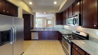 Located at 5611 Sirocco Lane in San Diego, CA, this two-story home offers a thoughtfully designed layout across both levels. The main living area is bright and welcoming, finished with plush carpeting and a ceiling fan, and opens directly onto a private balcony through a full-width sliding glass door, allowing natural light to pour in and providing access to outdoor views of surrounding greenery.

The kitchen is a standout feature, showcasing rich dark wood cabinetry, granite-style countertops, and a full suite of stainless steel appliances including a gas range, built-in microwave, dishwasher, and refrigerator. Light tile flooring and recessed lighting give the kitchen a clean, polished feel, and a pass-through window connects it to the adjacent living space.

The bedrooms are carpeted and generously sized, each offering ceiling fans and ample natural light through slatted window blinds. One bedroom includes a sliding glass door and direct access to a stairway landing area.

The bathrooms are well-finished, featuring dark wood vanities with granite countertops, tile flooring, and tub/shower combinations. The primary bathroom includes a dual-sink vanity, a separate walk-in closet area, and a dedicated shower space. Throughout the home, warm neutral tones and recessed lighting create a cohesive and comfortable atmosphere.
