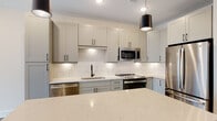 Located at 721 Halifax St in Raleigh, NC, this single-floor residence offers a thoughtfully designed layout with contemporary finishes throughout. The open-concept kitchen serves as the heart of the home, showcasing soft gray shaker cabinetry with matte black hardware, a white subway tile backsplash, and a generous quartz island with subtle veining. Stainless steel appliances—including a refrigerator, range, microwave, and dishwasher—complete the space, while pendant lighting adds a modern accent. The kitchen flows seamlessly into the living area, which features wood-look flooring, recessed lighting, and large French doors that invite natural light and provide access to the outdoors. The bedrooms are comfortable and well-proportioned, with wood-look flooring, ceiling fans, and ample natural light from well-placed windows. Generous walk-in closets with built-in shelving provide abundant storage. The bathroom is elegantly appointed with a frameless glass walk-in shower, white subway tile surround, matte black fixtures, a rain showerhead, and a quartz vanity top set over neutral tile flooring. Clean lines, neutral tones, and quality materials define the overall ambiance of this well-appointed Raleigh residence.