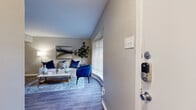 This single-story, one-bedroom, one-bathroom unit is thoughtfully designed to maximize every square foot of its compact footprint. The entrance opens directly into a bright and stylish living room featuring wood-look flooring, large windows with horizontal blinds that invite natural light, and neutral-toned walls. The space is anchored by a built-in shelving unit and complemented by a decorative sunburst mirror, giving the room a modern, curated feel.

Adjacent to the living room, the dining area accommodates a round four-seat table beneath a ceiling fan, with an open pass-through connecting seamlessly to the kitchen. The kitchen is equipped with white cabinetry, light countertops, black appliances including a gas range and refrigerator, and a peninsula that doubles as additional prep and serving space.

The bedroom is generously proportioned, featuring a ceiling fan with light fixture, a tray ceiling detail, a large window, and dual closets offering ample storage. Wood-look flooring continues throughout, maintaining visual consistency across the unit.

The bathroom includes a combination tub-shower, vanity with storage cabinetry, and textured wall accents. Black hardware details add a contemporary touch. The overall ambiance is modern and cohesive, with warm tones and practical finishes throughout.