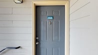 This single-floor residence features two bedrooms and two bathrooms within a thoughtfully designed layout. The entry is marked by a classic six-panel door in slate gray, framed by light siding and a cream trim, creating a clean and welcoming first impression.

Inside, a carpeted hallway connects the main living areas, finished with warm dark-brown door and window trim that contrasts neatly against the white walls. The interior benefits from natural light filtering through windows visible at the end of the corridor, giving the space an open and airy feel. Ceiling-mounted HVAC vents are integrated cleanly into the layout, ensuring year-round comfort. The neutral color palette throughout provides a versatile backdrop suitable for a variety of décor styles.

One of the standout features of this residence is the private balcony, supported by a sturdy wooden pergola post and enclosed by metal railings. The balcony overlooks a landscaped community courtyard with mature trees, parking areas, and neighboring brick-and-stone buildings, offering a pleasant outdoor retreat. The overall ambiance of the space is functional, tidy, and well-maintained.