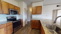 This single-floor residence offers a thoughtfully designed layout that balances comfort and functionality. The kitchen is a standout feature, showcasing warm honey-toned wood cabinetry, granite countertops, a classic subway tile backsplash, and a full suite of stainless steel appliances including a range, microwave, and refrigerator. Dark hardwood-style flooring grounds the kitchen and dining areas, adding a rich contrast to the light-colored walls throughout.

The open living area seamlessly transitions between hardwood-style flooring and plush carpeting, creating distinct yet connected zones for dining and relaxing. A ceiling fan overhead and a sliding glass door lead to a private balcony, where views of the surrounding landscape can be enjoyed. Natural light filters generously through the sliding door and additional windows.

Both bedrooms are carpeted and well-lit, each equipped with a ceiling fan and a window fitted with blinds that allow for adjustable natural light. The bedrooms offer a calm, neutral atmosphere ideal for rest.

The bathrooms are finished with warm wood cabinetry, granite-style countertops, and tile accents. One bathroom features a tiled shower, while the other includes a full soaking tub with tile surround. Both are complemented by hardwood-style flooring, completing the cohesive aesthetic found throughout the residence.