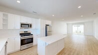 Located at 43808 Vintage St in Lancaster, CA, this modern single-story home offers a clean, contemporary design throughout. The open-concept kitchen and living area serves as the heart of the home, featuring white shaker cabinetry that extends to the ceiling, stainless steel appliances including a gas range, microwave, and refrigerator, and a central island with a crisp white countertop — all set atop light wood-tone flooring that runs seamlessly through the space. Natural light pours in through windows at the far end, enhancing the bright, airy ambiance. The three bedrooms are well-proportioned, with the generously sized primary bedroom offering ample space and access to closet storage. The two bathrooms are finished in a clean, white palette, with one featuring a glass-enclosed walk-in shower, white vanity, and a window for natural light. A versatile den provides flexible space for a home office or additional living area. The attached garage includes an automatic opener and a window for ventilation. Outside, the covered patio overlooks a low-maintenance backyard with artificial turf, decorative gravel, and desert-friendly plantings — ideal for the Lancaster climate. A dedicated laundry area and four closets round out this well-appointed home.