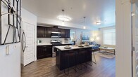 This single-floor residence is thoughtfully designed with an open-concept layout that seamlessly connects the kitchen, dining, and living areas. The kitchen is a standout feature, showcasing rich dark cabinetry paired with crisp white countertops, stainless steel appliances including a gas range, microwave, dishwasher, and refrigerator, and a central island with bar seating. Pendant and flush-mount lighting illuminate the space, while wood-look flooring extends throughout the main living areas, adding warmth and continuity.

The living area offers a comfortable, inviting atmosphere with natural light filtering in through windows fitted with horizontal blinds. The bedrooms are carpeted and well-sized, each benefiting from ample natural light. One bedroom features floor-to-ceiling vertical blinds, while another includes a dedicated walk-in closet with built-in shelving and hanging rods, providing generous storage.

The bathroom is finished with the same dark cabinetry and white countertop combination found in the kitchen, a wide vanity mirror, and wood-look flooring. Throughout the residence, a cohesive neutral color palette and consistent design language create a clean, modern ambiance.