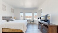 Located at 1659 Ocean Front Walk in Santa Monica, CA, this efficiently designed one-bedroom, one-bathroom unit offers a bright and clean coastal living experience. The space is finished throughout with light wood-tone flooring and crisp white walls, creating an airy, cohesive aesthetic.

The bedroom serves as the primary living area and is the most spacious room in the unit. A prominent bay window configuration allows abundant natural light to fill the room while framing views of the surrounding neighborhood. A mirrored sliding closet door enhances the sense of openness. The room comfortably accommodates a full bed, a media console with a flat-screen television, and a small desk-and-chair arrangement positioned near the windows.

The kitchen is efficiently laid out with white upper cabinetry, dark stone countertops, and light wood flooring that continues from the main room. It is equipped with a stainless steel range and a microwave, making it fully functional despite its compact footprint. A window above the counter provides additional natural light.

The bathroom features a full tub-and-shower combination with clean white subway tile surround and chrome fixtures, maintaining the simple, well-maintained character found throughout the unit. Overall, this space offers a practical and comfortable layout in a prime beachside Santa Monica location.