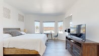 Located at 1659 Ocean Front Walk in Santa Monica, CA, this efficiently designed one-bedroom, one-bathroom unit offers a bright and clean coastal living experience. The space is finished throughout with light wood-tone flooring and crisp white walls, creating an airy, cohesive aesthetic.

The bedroom serves as the primary living area and is the most spacious room in the unit. A prominent bay window configuration allows abundant natural light to fill the room while framing views of the surrounding neighborhood. A mirrored sliding closet door enhances the sense of openness. The room comfortably accommodates a full bed, a media console with a flat-screen television, and a small desk-and-chair arrangement positioned near the windows.

The kitchen is efficiently laid out with white upper cabinetry, dark stone countertops, and light wood flooring that continues from the main room. It is equipped with a stainless steel range and a microwave, making it fully functional despite its compact footprint. A window above the counter provides additional natural light.

The bathroom features a full tub-and-shower combination with clean white subway tile surround and chrome fixtures, maintaining the simple, well-maintained character found throughout the unit. Overall, this space offers a practical and comfortable layout in a prime beachside Santa Monica location.