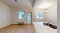 This single-floor residence offers a clean, modern aesthetic throughout, combining functional design with comfortable living spaces. The open-concept living and dining area is highlighted by striking vaulted ceilings and warm light wood laminate flooring that extends seamlessly through the home. Multiple windows fill the space with natural light, and a ceiling fan adds to the airy feel. A glass-paneled exterior door connects the living area to the outdoors. The kitchen features a galley-style layout with light wood cabinetry, sleek white countertops, and a full suite of black appliances including a refrigerator, electric range, and over-the-range microwave. A kitchen island provides additional counter space and overlooks the main living area. The bedroom is generously proportioned, benefiting from natural light through a large window and offering a built-in closet with sliding doors for ample storage. The bathroom is a standout feature, adorned with decorative patterned floor tile, light wood vanity cabinetry, a white countertop, and a bathtub-shower combination. Neutral tones and clean lines are carried throughout the home, creating a cohesive and inviting atmosphere that is both modern and practical.