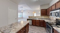 Located at 245 Creekwood Cove Lane in Lenoir City, Tennessee, this single-story, 3-bedroom, 2-bathroom home offers a comfortable and functional layout. The kitchen is a standout feature, showcasing rich dark wood cabinetry, granite-style countertops, a center island, tile backsplash, and stainless steel appliances. It opens seamlessly into the living area, which benefits from a vaulted ceiling with a ceiling fan and natural light from multiple windows. An arched architectural detail adds a decorative touch to the transition between spaces. The bedrooms are carpeted and well-lit, with the primary bedroom offering generous proportions and ample natural light through multiple windows. Three closets are distributed throughout the home, including a spacious walk-in closet equipped with wire shelving and a separate rack system for organized storage. Both bathrooms feature tiled flooring, a tub-shower combination with mosaic tile surround, and dark wood vanities. A dedicated laundry room with side-by-side washer and dryer hookups and wood-look flooring adds everyday convenience. Throughout the home, neutral tones and clean finishes create a bright, move-in-ready atmosphere.