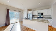 Located at 49 Wildcat Dr. in Rochester, NH, this two-story home offers a thoughtfully designed layout spread across two well-proportioned floors. The main level features an open-concept kitchen and living area anchored by warm, natural hardwood flooring that flows throughout. The kitchen is a standout, showcasing white shaker-style cabinetry, granite countertops, a large central island with a sink, and a full suite of stainless steel appliances including a gas range, built-in microwave, and French door refrigerator. Recessed lighting and a sliding glass door to the exterior fill the space with natural light and provide seamless indoor-outdoor access. The expansive living area offers generous open space, ideal for flexible furniture arrangements. Upstairs, four bedrooms provide ample accommodation, including a generously sized primary bedroom featuring three large windows that flood the room with natural light. The primary suite includes a walk-in closet and a private bathroom. Additional bedrooms are well-sized with clean, neutral finishes and hardwood floors throughout. A hallway and dedicated closet space complete the upper level. The home's consistent use of light tones, clean lines, and quality materials creates a bright, modern, and welcoming ambiance throughout.