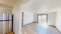 This single-floor residence has been thoughtfully renovated throughout, combining clean, contemporary finishes with a comfortable, functional layout. Light-toned hardwood flooring runs through the main living areas, complementing crisp white walls, gray baseboards, and textured ceilings that add subtle depth to each room.

The living area is bright and open, benefiting from generous natural light that streams in through a large sliding glass door leading to a wood-railed outdoor deck. The seamless connection between the interior and exterior creates a welcoming sense of openness.

The kitchen is well-appointed with gray shaker-style cabinetry, gold hardware accents, granite-look countertops, a stainless steel appliance suite including a range, over-the-range microwave, and refrigerator, as well as a gold-finish sink faucet — delivering a cohesive, modern aesthetic.

Bedrooms are finished with plush neutral carpeting and feature windows that allow natural light to fill the space. One bedroom includes a dedicated closet with built-in shelving, providing practical storage. A secondary room with hardwood flooring offers versatility as an office or additional living space.

The bathroom is clean and modern, featuring a tiled tub-shower surround with matte black fixtures, hardwood flooring, and a white vanity, creating a fresh, minimal aesthetic throughout.