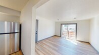 This single-floor residence has been thoughtfully renovated throughout, combining clean, contemporary finishes with a comfortable, functional layout. Light-toned hardwood flooring runs through the main living areas, complementing crisp white walls, gray baseboards, and textured ceilings that add subtle depth to each room.

The living area is bright and open, benefiting from generous natural light that streams in through a large sliding glass door leading to a wood-railed outdoor deck. The seamless connection between the interior and exterior creates a welcoming sense of openness.

The kitchen is well-appointed with gray shaker-style cabinetry, gold hardware accents, granite-look countertops, a stainless steel appliance suite including a range, over-the-range microwave, and refrigerator, as well as a gold-finish sink faucet — delivering a cohesive, modern aesthetic.

Bedrooms are finished with plush neutral carpeting and feature windows that allow natural light to fill the space. One bedroom includes a dedicated closet with built-in shelving, providing practical storage. A secondary room with hardwood flooring offers versatility as an office or additional living space.

The bathroom is clean and modern, featuring a tiled tub-shower surround with matte black fixtures, hardwood flooring, and a white vanity, creating a fresh, minimal aesthetic throughout.