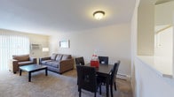 This two-floor residence offers a thoughtfully arranged layout designed for comfortable everyday living. The main level features an open living and dining area with soft carpeting, neutral walls, and a flush ceiling light that creates a warm, welcoming atmosphere. The living room provides generous seating space and is anchored by a large sliding glass door dressed in vertical blinds, allowing ample natural light and outdoor views. Adjacent to it, the dining area accommodates a full-sized table and chairs, ideal for meals and gatherings. A staircase connects the levels, with the kitchen conveniently positioned nearby on the main floor. The galley-style kitchen is efficiently designed with white cabinetry, dark countertops, a full-size refrigerator, dishwasher, and wood-look flooring that adds a clean, modern touch. A half bathroom on this level features a classic pedestal sink, a mirror with vanity lighting, and the same wood-look flooring. The upper level hosts two well-proportioned bedrooms, each carpeted and finished in soft, neutral tones. Both offer ample storage and natural light. A full bathroom with a tub/shower combination, white vanity cabinetry, and wood-look flooring serves the upper level. Throughout, the space maintains a clean, understated aesthetic suited for practical, day-to-day living.