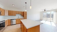 Located in Baraboo, Wisconsin, this well-appointed one-bedroom, one-bathroom unit offers a thoughtfully designed open-concept layout that maximizes its comfortable living space. Light-toned hardwood-style flooring runs throughout the main living areas, creating a cohesive and clean aesthetic.

The kitchen is a standout feature, equipped with warm wood cabinetry, stainless steel appliances including a refrigerator, range, microwave, and dishwasher, and a generous center island with a white countertop that doubles as additional prep and dining space. Pendant lighting above the island adds a stylish touch. The kitchen flows seamlessly into the bright living area, which is anchored by a ceiling fan and sliding glass doors that open to a private balcony overlooking a natural outdoor setting.

The bedroom is a comfortable, carpeted retreat filled with natural light from a large window, also fitted with a ceiling fan. A dedicated closet provides convenient storage.

The bathroom is finished with matching wood cabinetry, a white countertop vanity, a wall-mounted medicine cabinet, a large mirror, and a glass-enclosed walk-in shower with tile surround and light hardwood-style flooring. The overall palette of white walls and warm wood tones gives the space a clean, modern, and welcoming ambiance throughout.