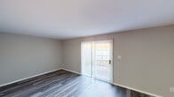 This two-floor space is designed with a clean, neutral aesthetic throughout, combining functionality with a straightforward, comfortable layout. The main living area features durable wood-look plank flooring in a cool gray tone and is anchored by a sliding glass door dressed with vertical blinds, which floods the room with natural light and provides direct access to an outdoor space. An additional room with matching wood-look flooring offers flexible use as a dining or secondary living area.

The kitchen is outfitted with gray flat-front cabinetry, brushed nickel hardware, white countertops, a stainless steel double-basin sink, and a gas range, providing a practical and modern cooking environment. Light wood-look flooring carries through this space, complementing the cabinetry.

Carpeted bedrooms are bright and well-proportioned, each featuring windows with horizontal blinds that allow controllable natural light. The neutral gray walls and textured ceilings are consistent throughout the upper level.

Two bathrooms serve the space: one features a shower stall with white tile surround and a vanity with mirror, while the second includes a full soaking tub and shower combination with white tile, maintaining a clean and minimal appearance throughout.
