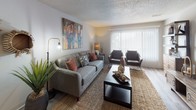 Located at 201 N Academy Blvd in Colorado Springs, Colorado, this single-floor residence offers a thoughtfully designed layout with a warm, rustic-modern aesthetic throughout. The living room serves as a central gathering space, featuring wood-look flooring, a large sliding glass door that welcomes natural light, and room for comfortable seating arrangements. The galley-style kitchen is equipped with white cabinetry, speckled light countertops, track lighting, and appliances including a full-size refrigerator and dishwasher, all set atop light wood-look flooring. Adjacent to the kitchen, the dining area accommodates a solid wood table with industrial-style seating, accented by a ceiling fan with lighting and decorative wall art. The space includes multiple bedrooms, each featuring closets with bifold doors, textured ceilings, and cozy carpet or hard-surface flooring. The bathroom includes a full tub-shower combination with clean white tile surround, wood-look flooring, and practical open shelving for storage. Throughout the residence, a cohesive earthy color palette with warm orange and navy accents creates an inviting and comfortable atmosphere suited to Colorado living.