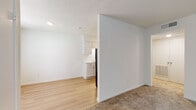 This single-floor unit offers a clean, functional layout designed to maximize everyday comfort and usability. The living area is spacious and open, featuring warm neutral carpet underfoot and crisp white walls throughout, creating a bright and inviting atmosphere. A textured ceiling adds a subtle architectural detail consistent across the main living spaces. The layout flows naturally from the carpeted living area into a connected zone where hardwood-style flooring transitions toward the kitchen, providing a clear distinction between spaces. The kitchen is well-equipped, featuring white cabinetry with modern hardware, light-toned countertops, and black appliances including an electric range with a range hood, offering a striking contrast against the cabinetry. A refrigerator is also present, making the kitchen move-in ready. The bedroom is generously proportioned, benefiting from two windows that allow ample natural light to fill the room, and is finished with soft carpeting for added comfort. A full bathroom serves the unit, complete with a tub and shower combination accented by tile surround, and hardwood-style flooring for easy maintenance. The entryway provides a welcoming transition into the unit, with a secondary door nearby offering additional storage or utility access. Overall, the space presents a straightforward, well-maintained interior with a neutral palette suited to a variety of personal styles.
